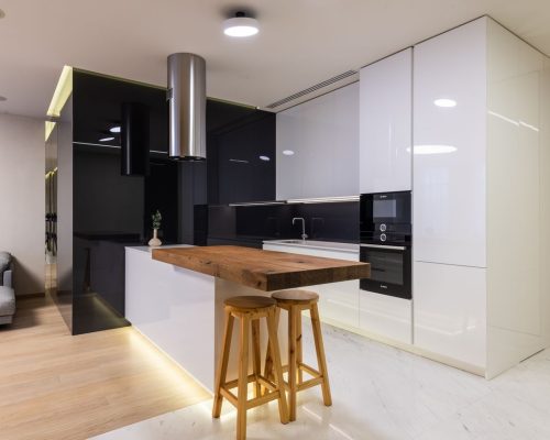 Interior of modern apartment with kitchen zone furnished with glossy cabinets and living area with sofa